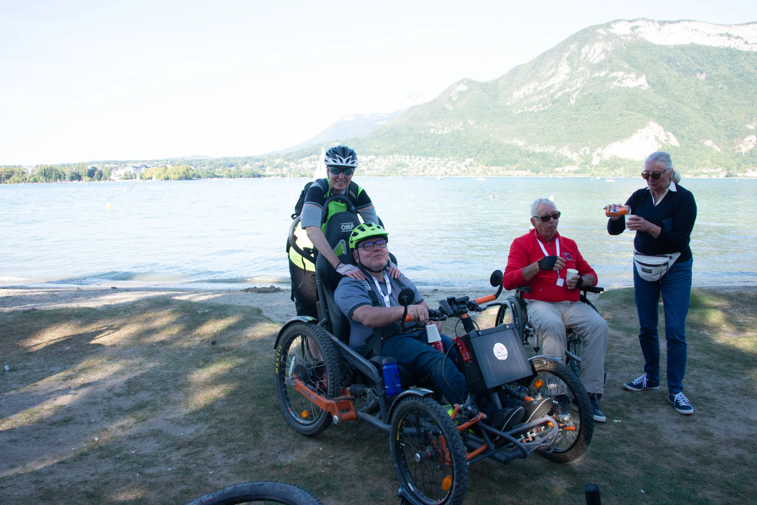Deux participants et une accompagnatrice devant le lac d'Annecy à l'arrivée de la descente du Semnoz lors du R'Handi Bike Festival