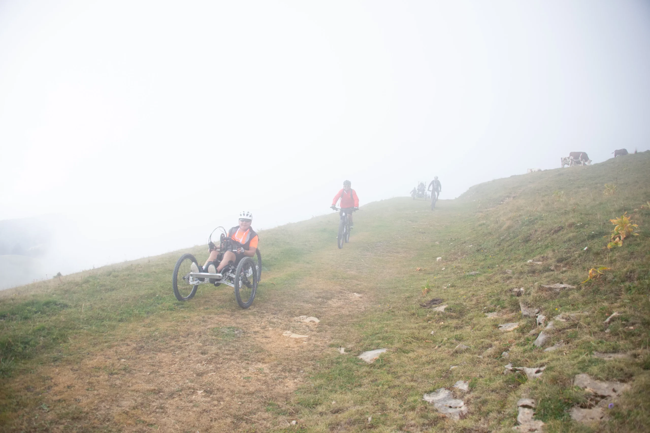 Un accompagnateur et un participant dans les nuages dans une descente sur chemin herbeux du Semnoz