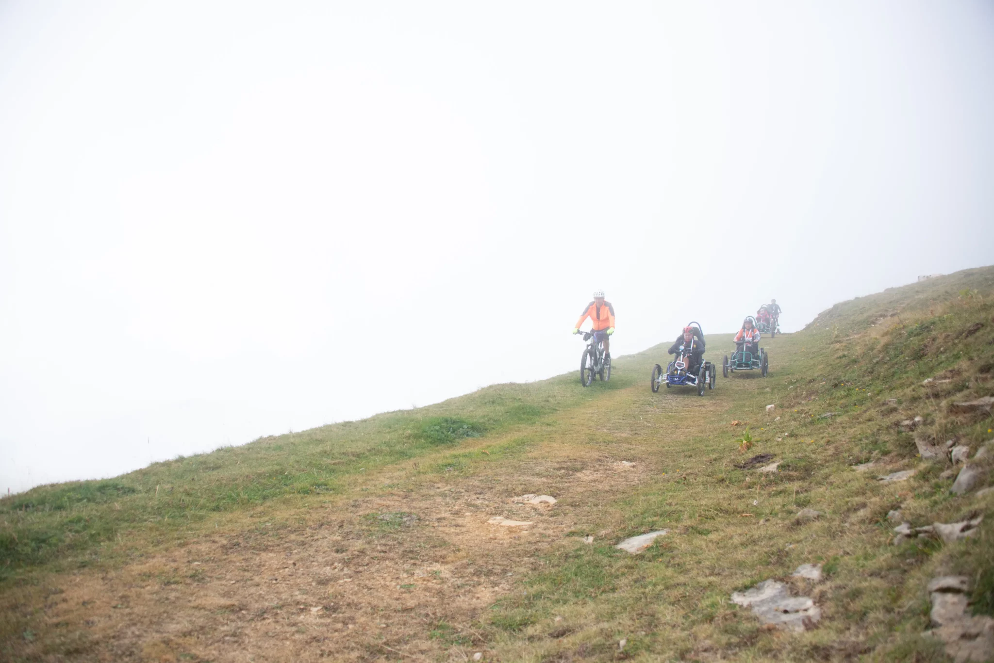 Trois participants en FTT et un accompagnateur dans les nuages dans une descente sur chemin herbeux du Semnoz