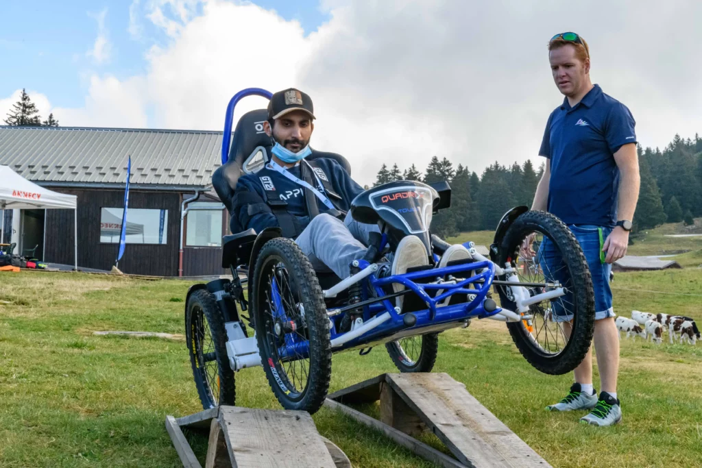 Un participant en fauteuil tout terrain qui teste le parcours de trial avec une roue en l'air lors du R'Handi Bike Festival