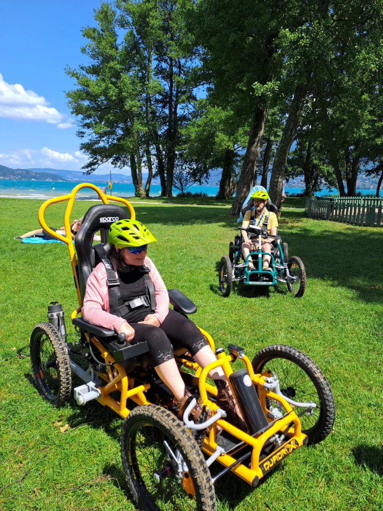 Sabine et Vincent, résidents de la Maisonnée du Lac, font une pause devant le lac d'Annecy avec des Quadrix de l'association Handi Lac & Montagnes