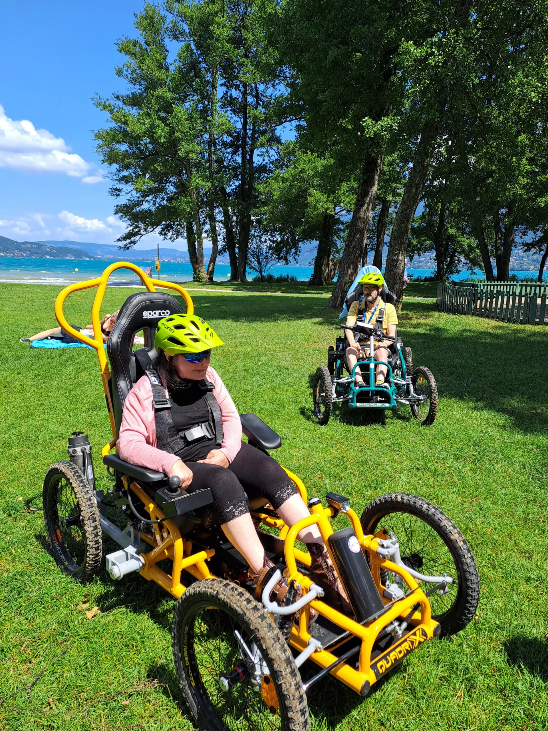 Sabine et Vincent, résidents de la Maisonnée du Lac, font une pause devant le lac d'Annecy avec des Quadrix de l'association Handi Lac & Montagnes