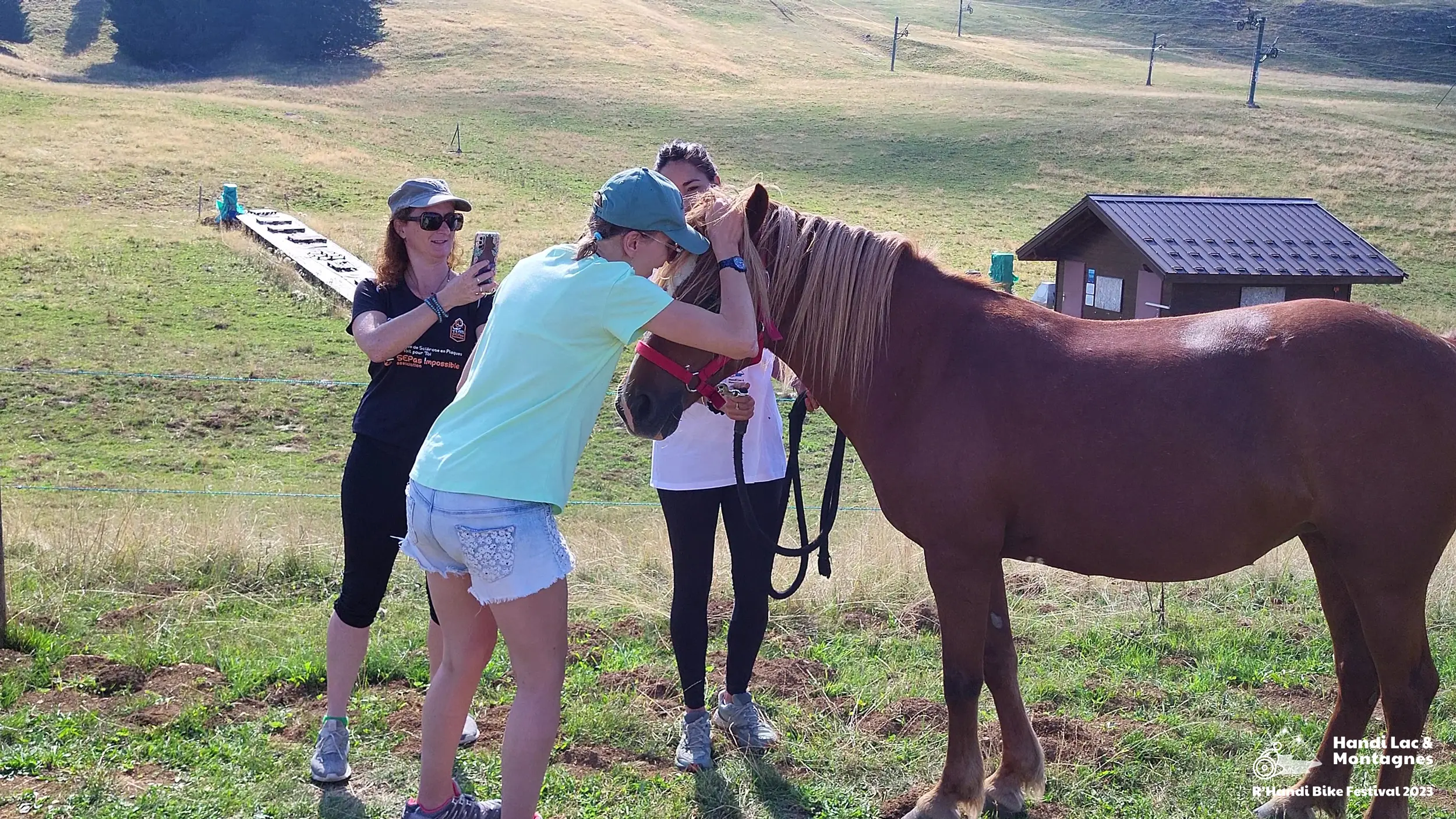 Une bénévole de Poils de Bonheur fait carresser son cheval à une jeune visiteuse du village du R'Handi Bike Festival 2023
