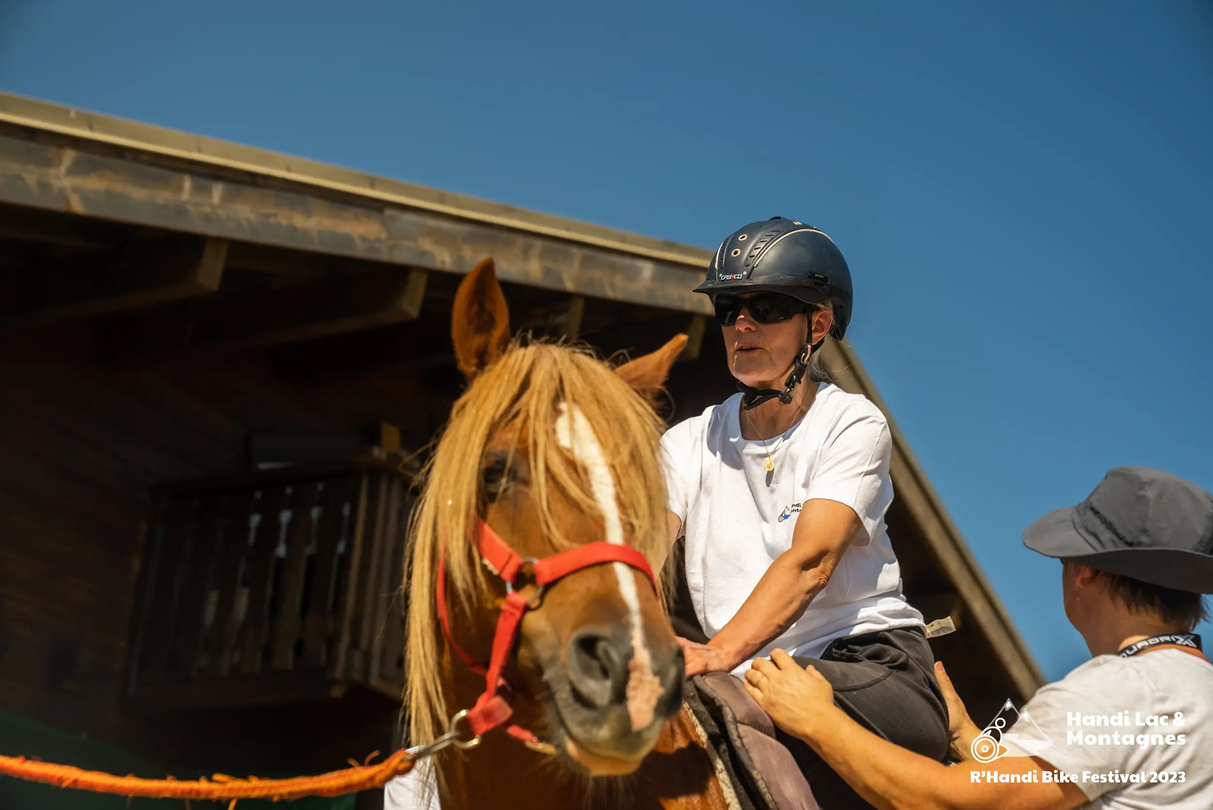 Une personne à mobilité réduite monte sur un cheval avec l'aide d'une bénévole