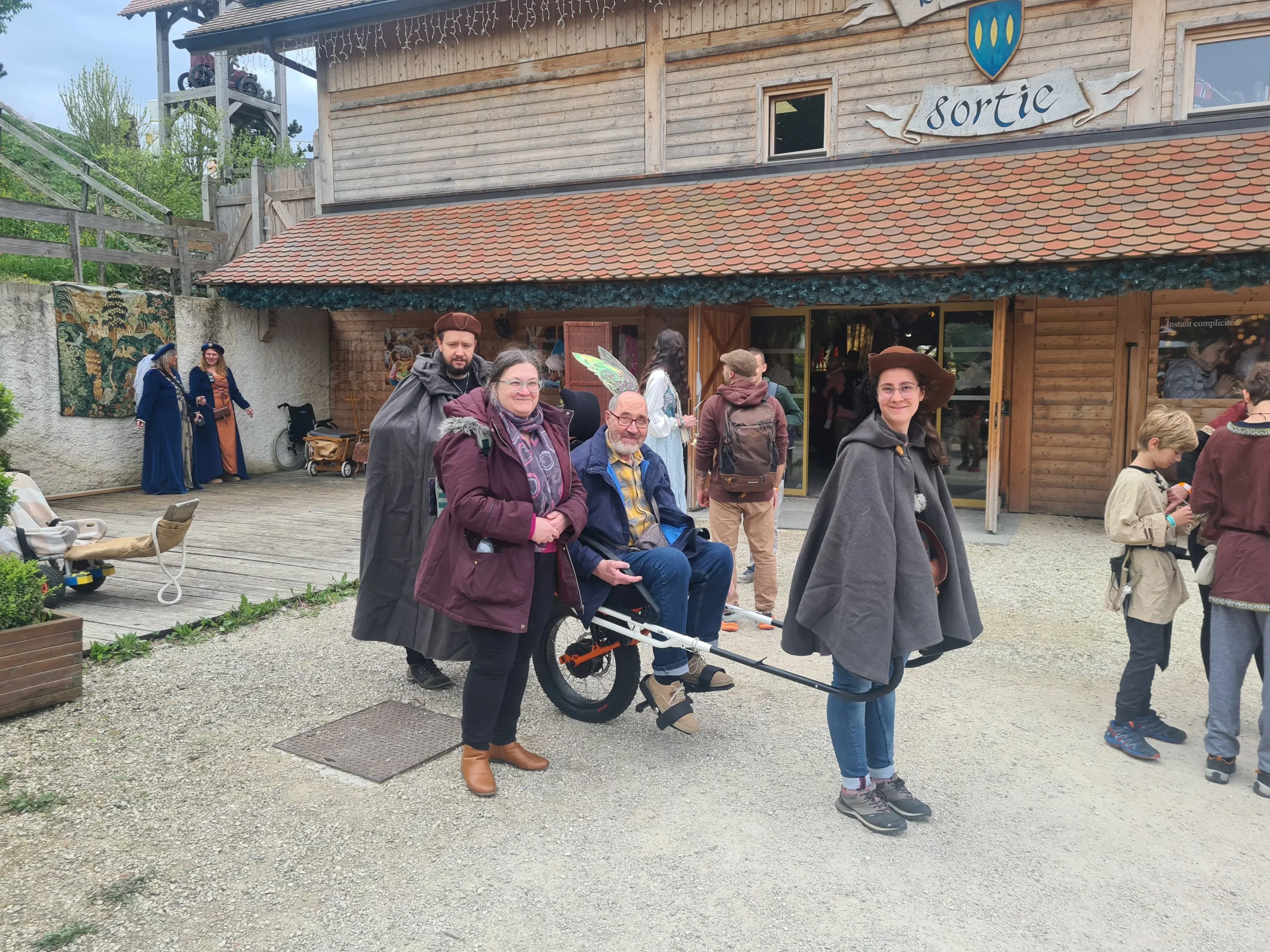 Deux accompagnateurs font découvrir les médiévales d'andilly à ce monsieur grâce à une joëlette de l'association Handi Lac & Montagnes