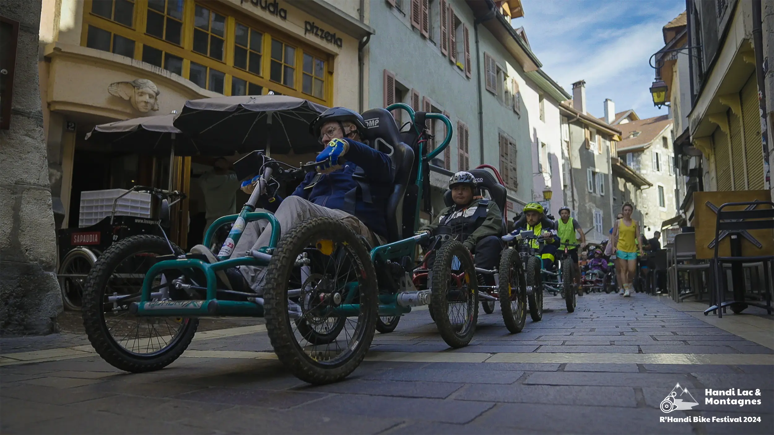 Des participants du R'Handi Bike Festival 2024 dans la vieille veille d'Annecy