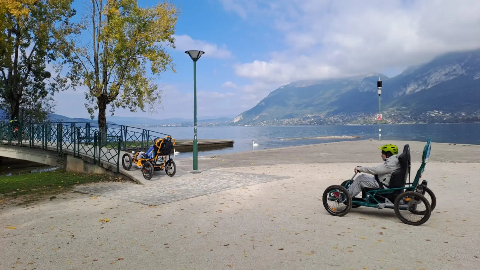 3 Quadrix de l'association Handi Lac & Montagnes franchissent une passerelle sur les bords du lac d'Annecy